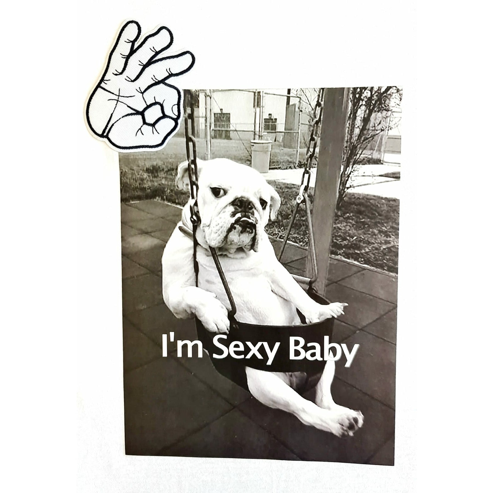 White t-shirt featuring a black and white graphic of a bulldog sitting on a swing with the text "I'm Sexy Baby" and a hand making an "OK" gesture above