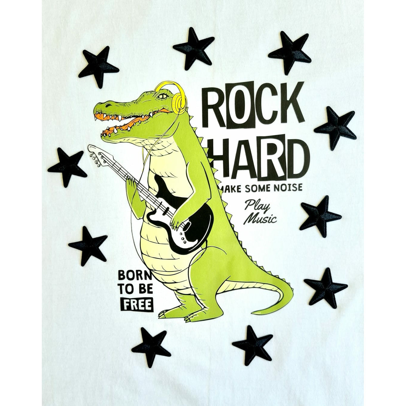 White t-shirt featuring a cartoon crocodile playing a guitar, surrounded by stars and the text "ROCK HARD," "MAKE SOME NOISE," "Play Music," and "BORN TO BE FREE"