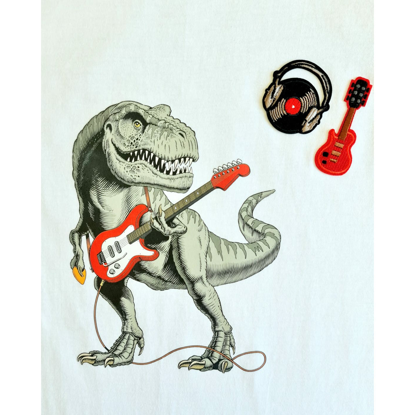 White t-shirt featuring a T-Rex playing a red electric guitar with additional graphics of a vinyl record and a small red guitar